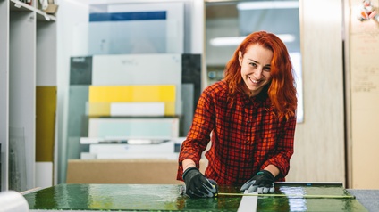 Lehrling lächelnd Glasscheibe auf Werkbank vermessend